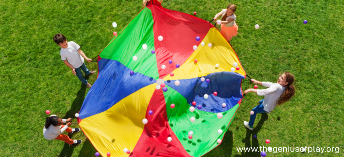 young children waving a large colorful parachute up in the air outdoors