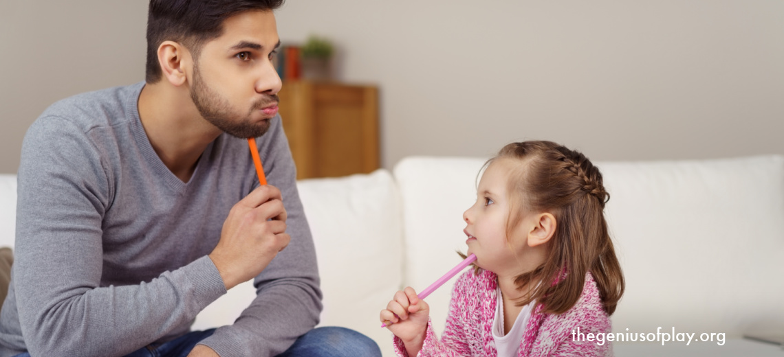 Adorable little girl mimicking her father holding a pencil to her chin with a thoughtful expression 